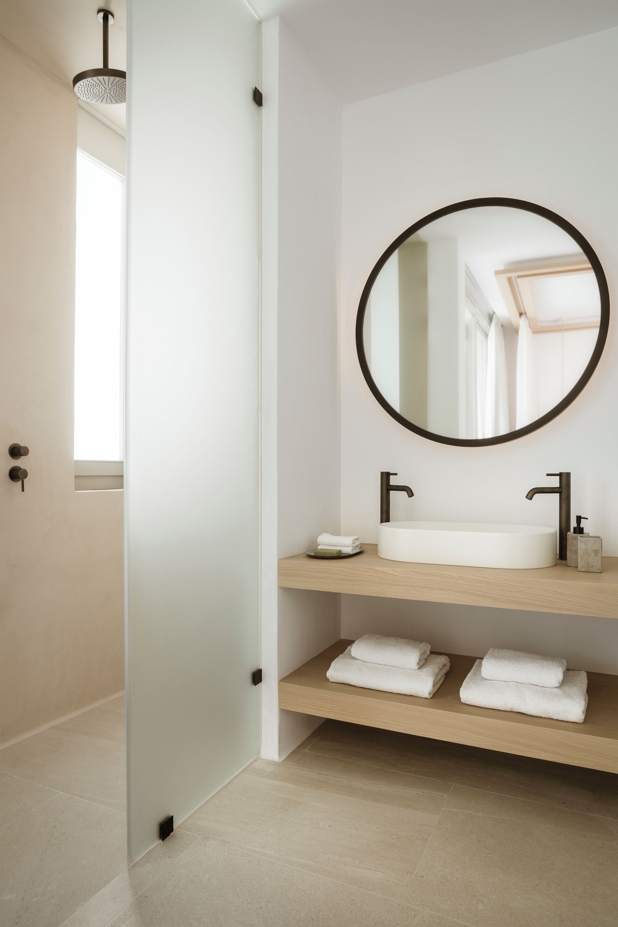 A bathroom with a round mirror, two sinks, and a towel rack.