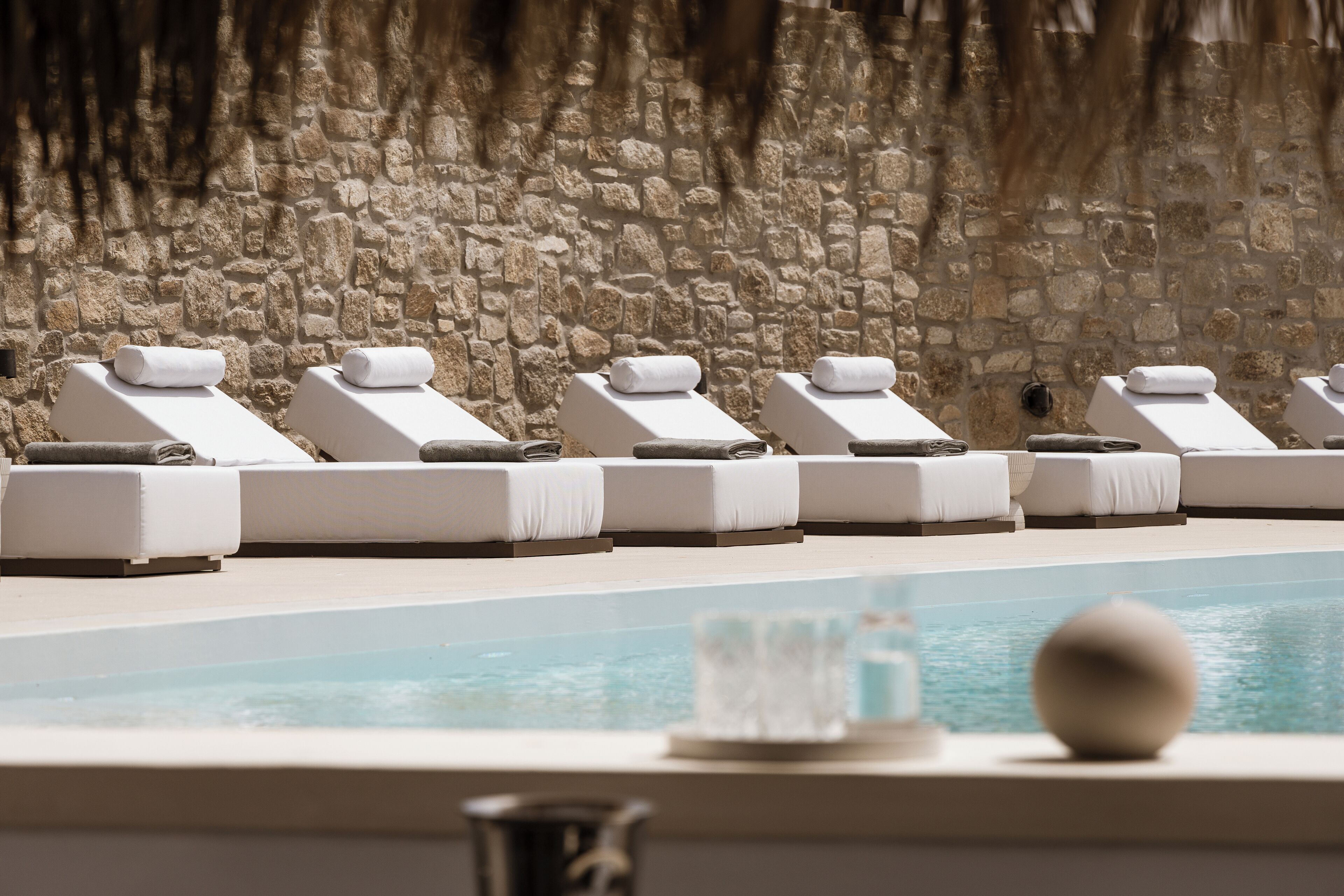 A poolside area with lounge chairs and a stone wall.