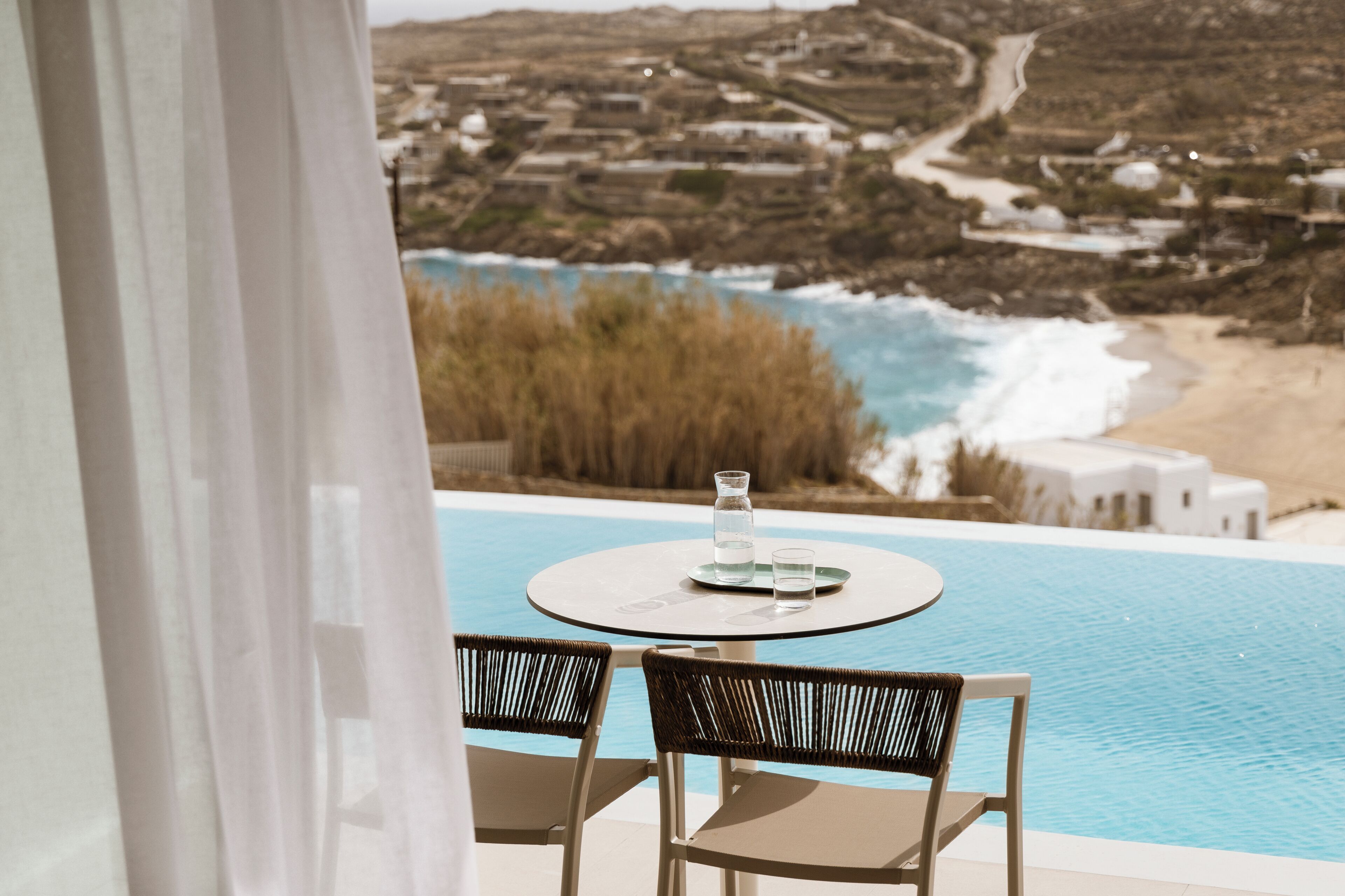 Vista de la piscina con una mesa y sillas, con vistas a una playa y al paisaje costero.