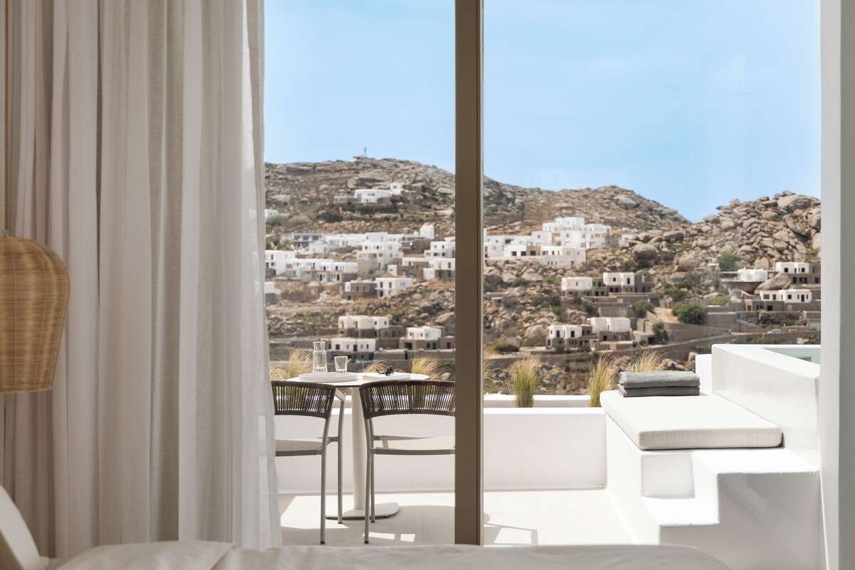 Un balcón con mesa y sillas, con vistas a un complejo de edificios blancos en una colina.