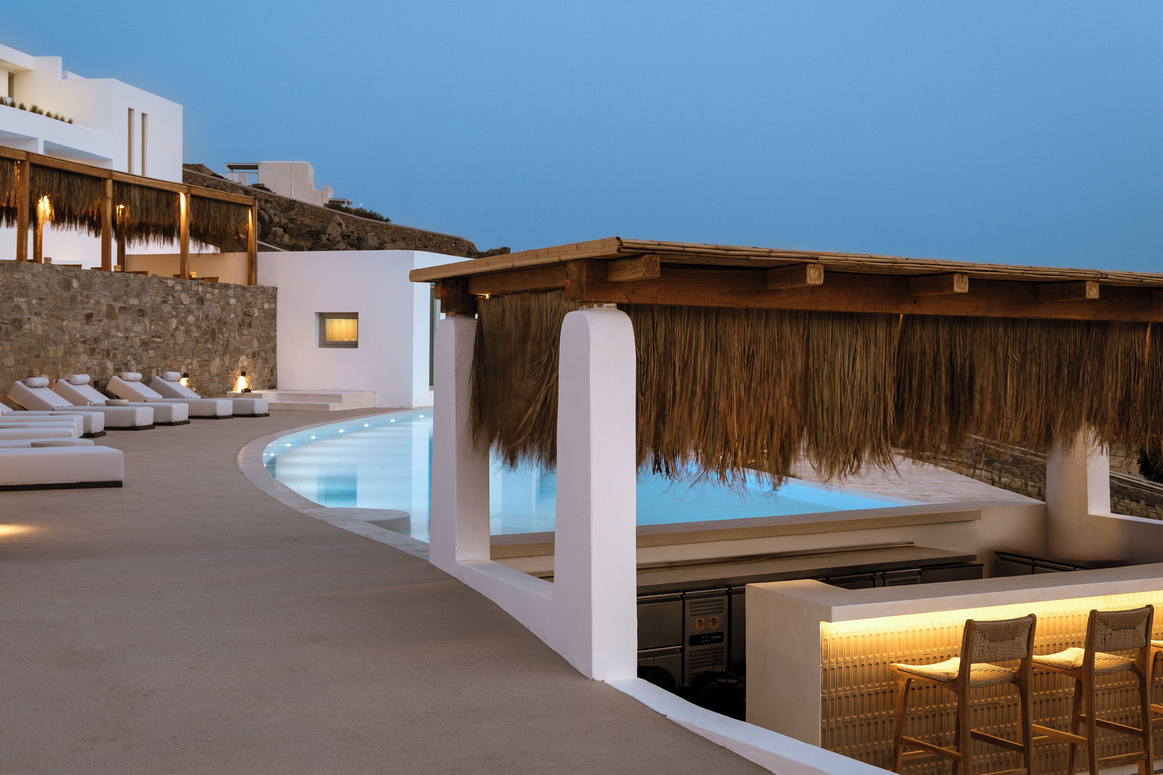 A poolside area with lounge chairs, a bar area, and a thatched roof structure.