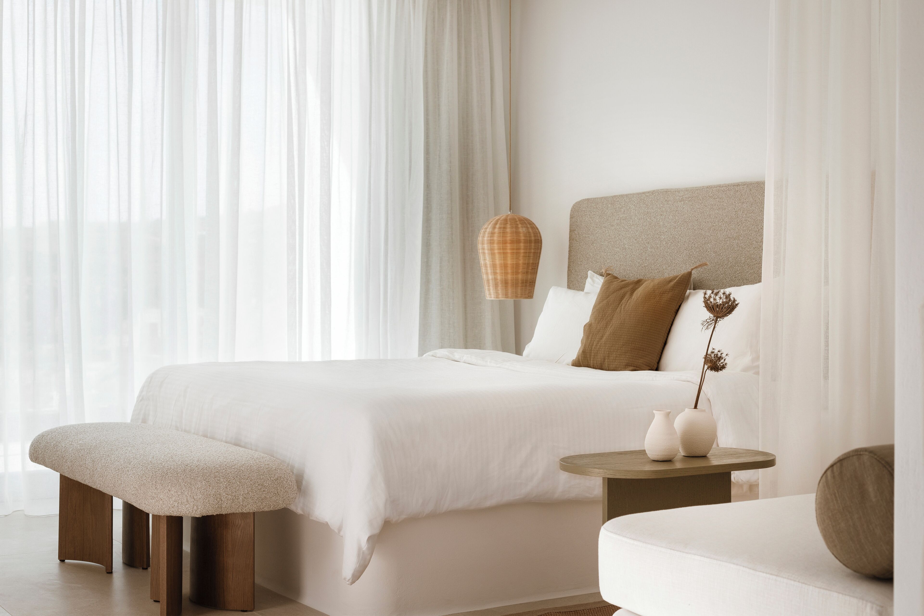 A modern bedroom with a large bed, bedside tables, a bench, and a hanging light fixture.