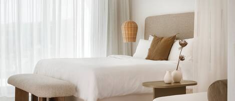 A modern bedroom with a large bed, bedside tables, a bench, and a hanging light fixture.