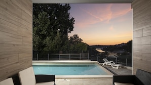 A modern outdoor pool area with lounge chairs and a view of the sunset over a residential area.