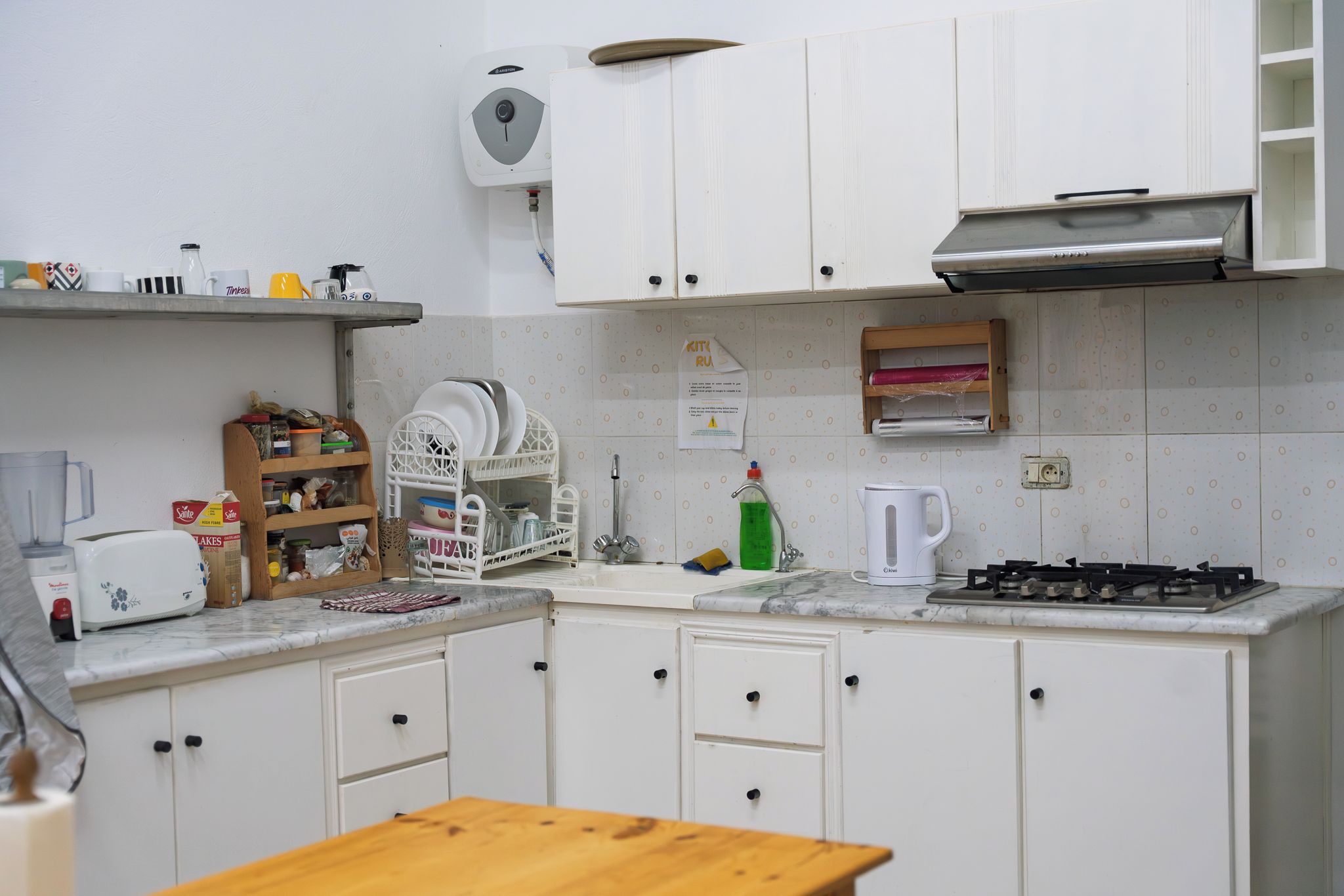Cocina compacta con armarios blancos, estufa a gas, cafetera y escurreplatos.