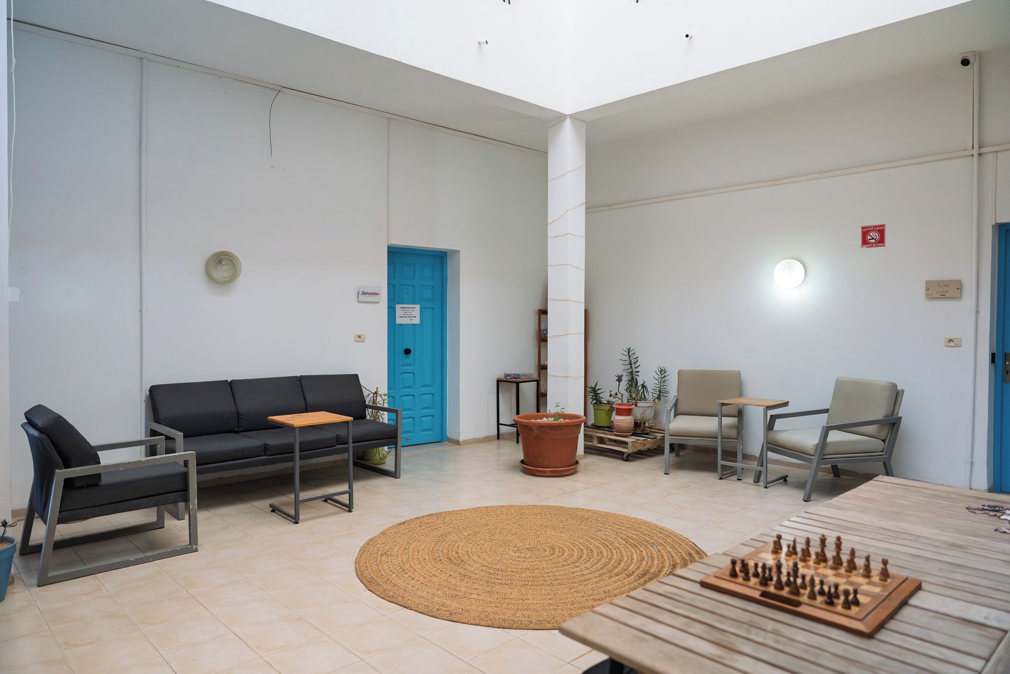 Un área de espera moderna con un sofá, sillas, una mesa de ajedrez y una puerta azul.