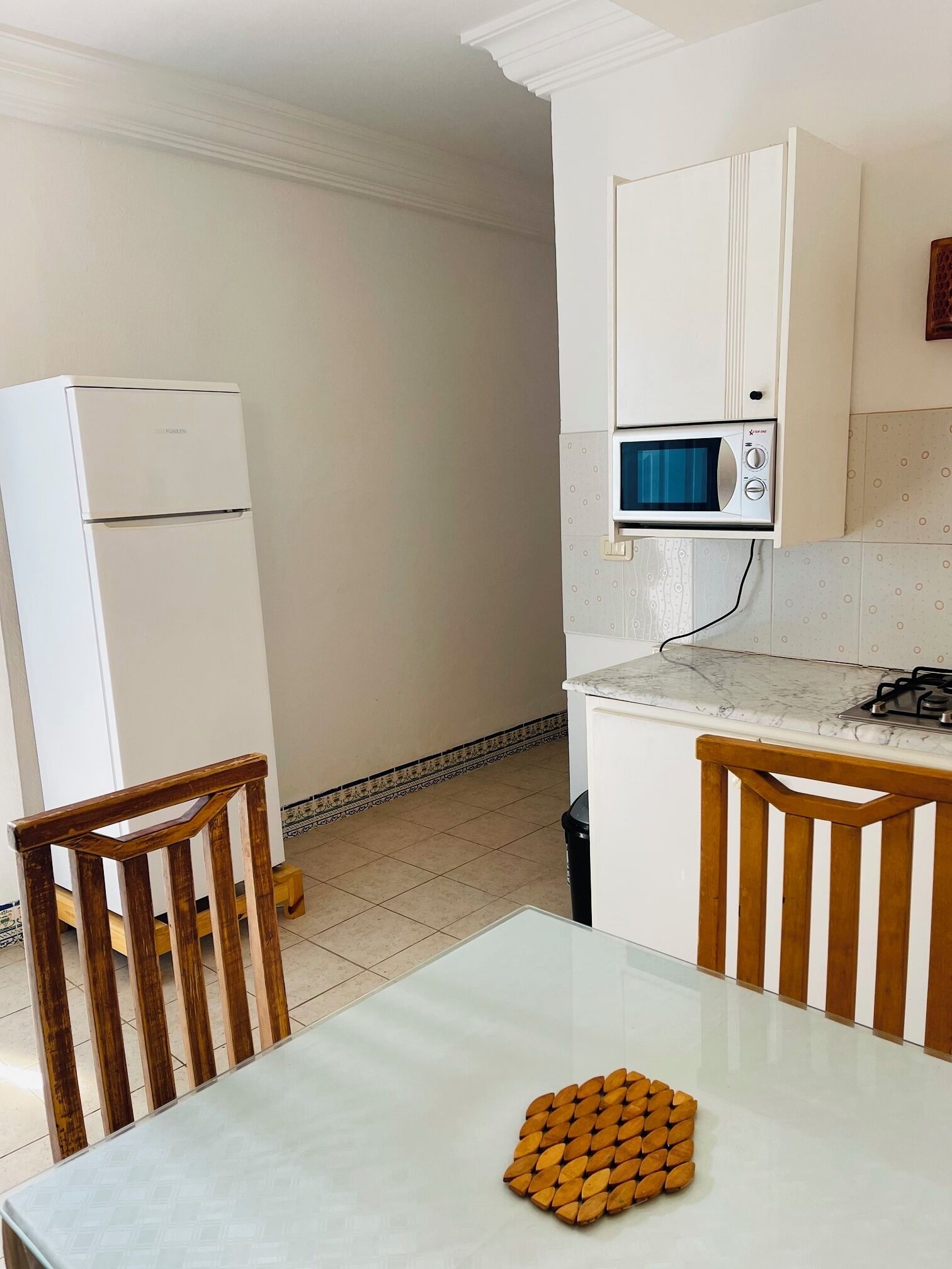 A compact kitchen with a refrigerator, microwave, and a small dining table with chairs.