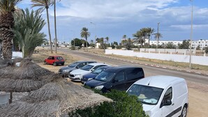 A parking area with several cars, a white van, and a small outdoor seating area with chairs and a table. - Cozi Coliving (Mezraia)