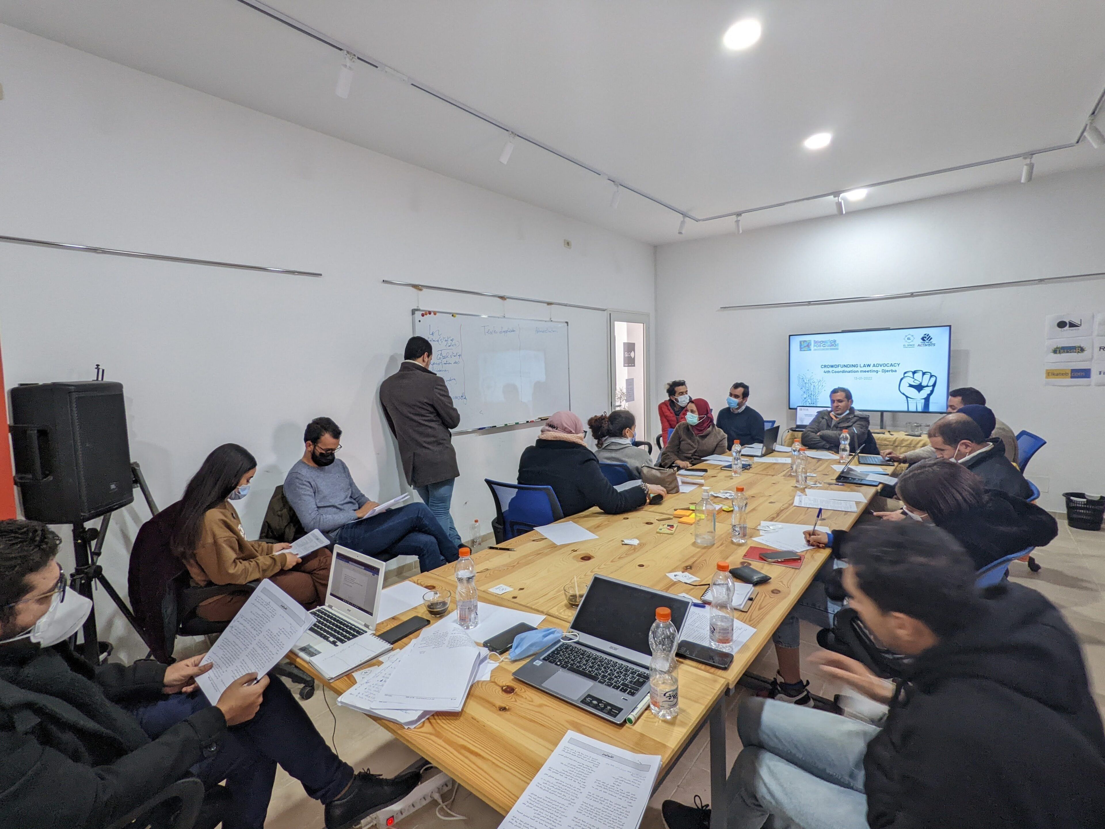 A conference room with a long table, laptops, papers, and a projector screen displaying a presentation.