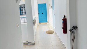 A hallway with a blue door at the end, a fire extinguisher, and a potted plant. - Cozi Coliving (Mezraia)