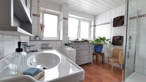 A modern bathroom with a large sink, a mirror, a window, a towel rack, and a potted plant. - Plant Apartment - Large balcony with barbecue (Eutingen im Gäu)