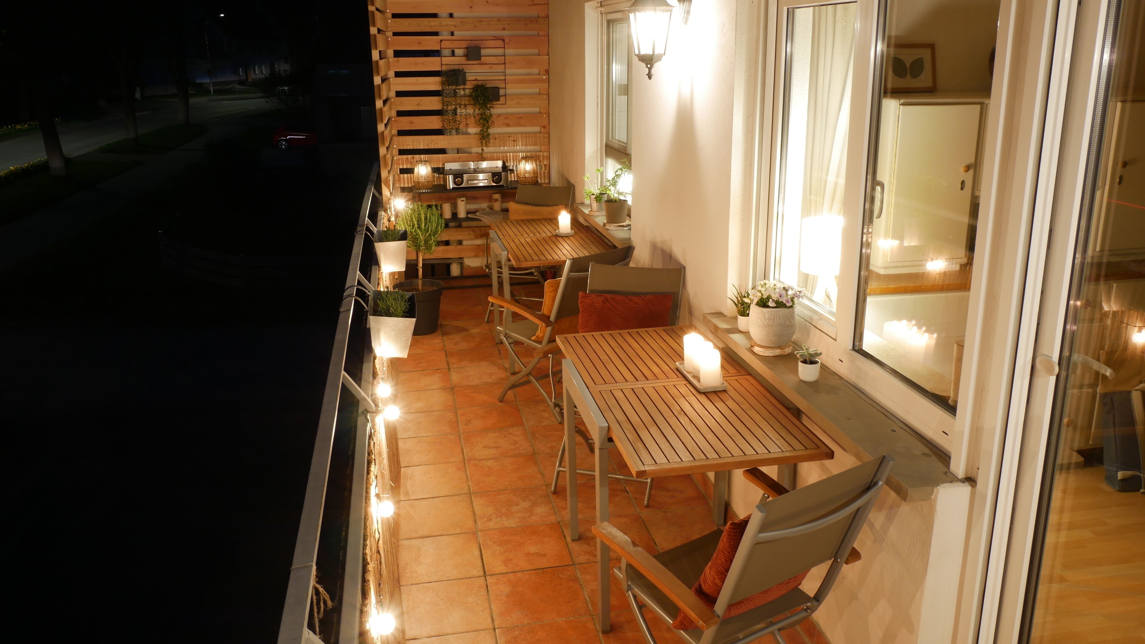 An outdoor patio with wooden tables and chairs, potted plants, and a street view in the background.