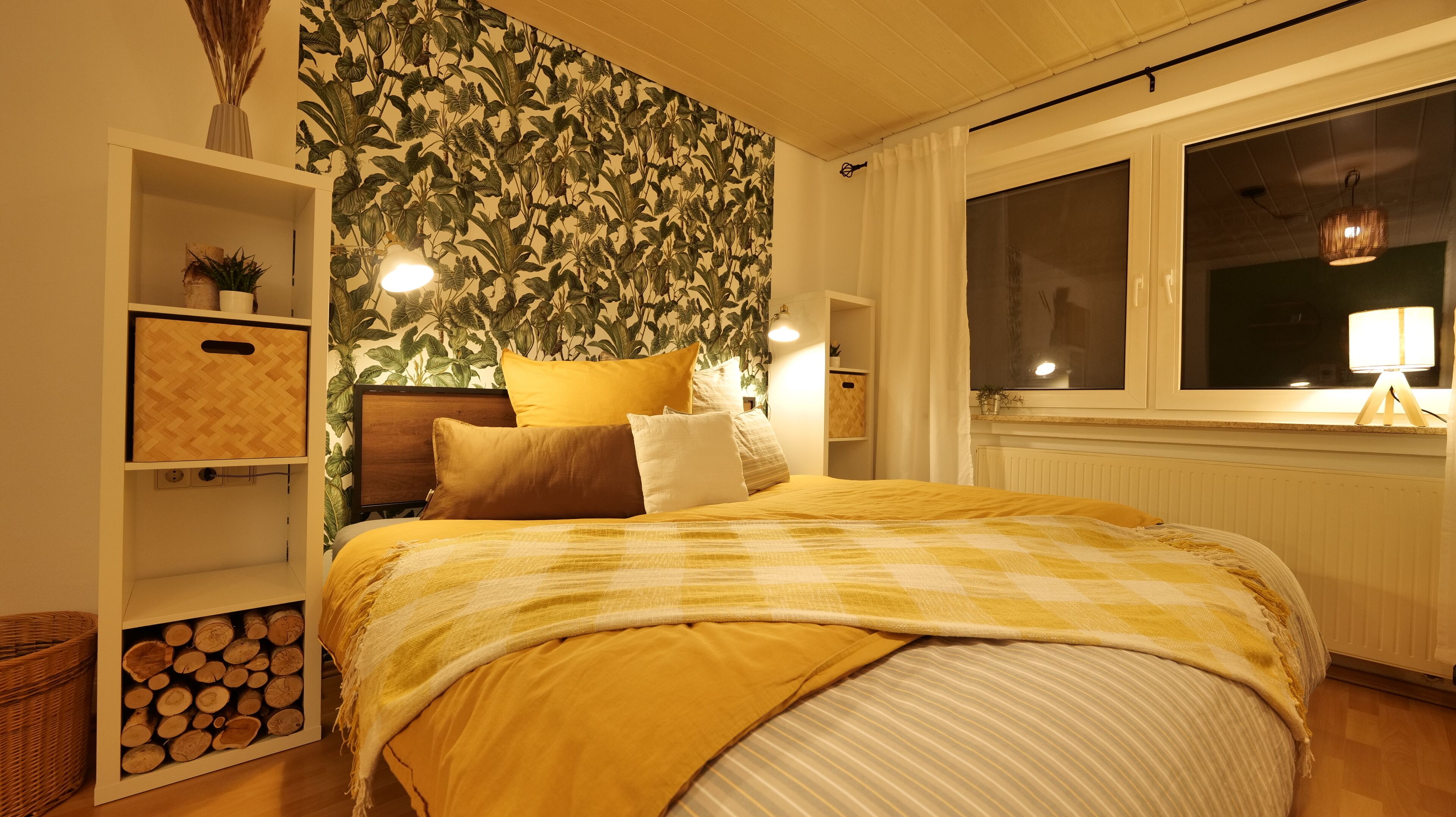 Una camera da letto con un letto, un comodino, una lampada, una finestra e una parete con un motivo a foglia.