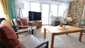 Un soggiorno moderno con un divano, un tavolino in legno con della frutta, una televisione e una poltrona in vimini.