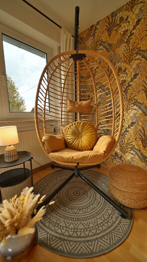 A room with a hanging chair, a lamp, a patterned rug, and a wall with a botanical wallpaper. - Plant Apartment - Large balcony with barbecue (Eutingen im Gäu)