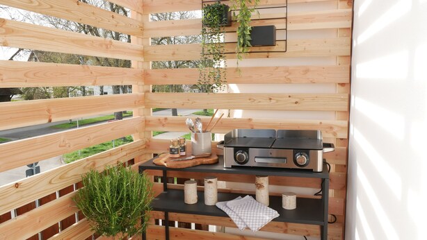 Cucina esterna in legno con barbecue, utensili da cucina e una pianta.