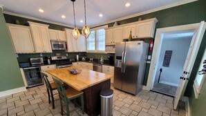 A kitchen with white cabinets, a stainless steel refrigerator, a wooden island, and a trash can.