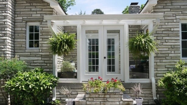 A stone house with a covered front porch, two windows, and potted plants.
