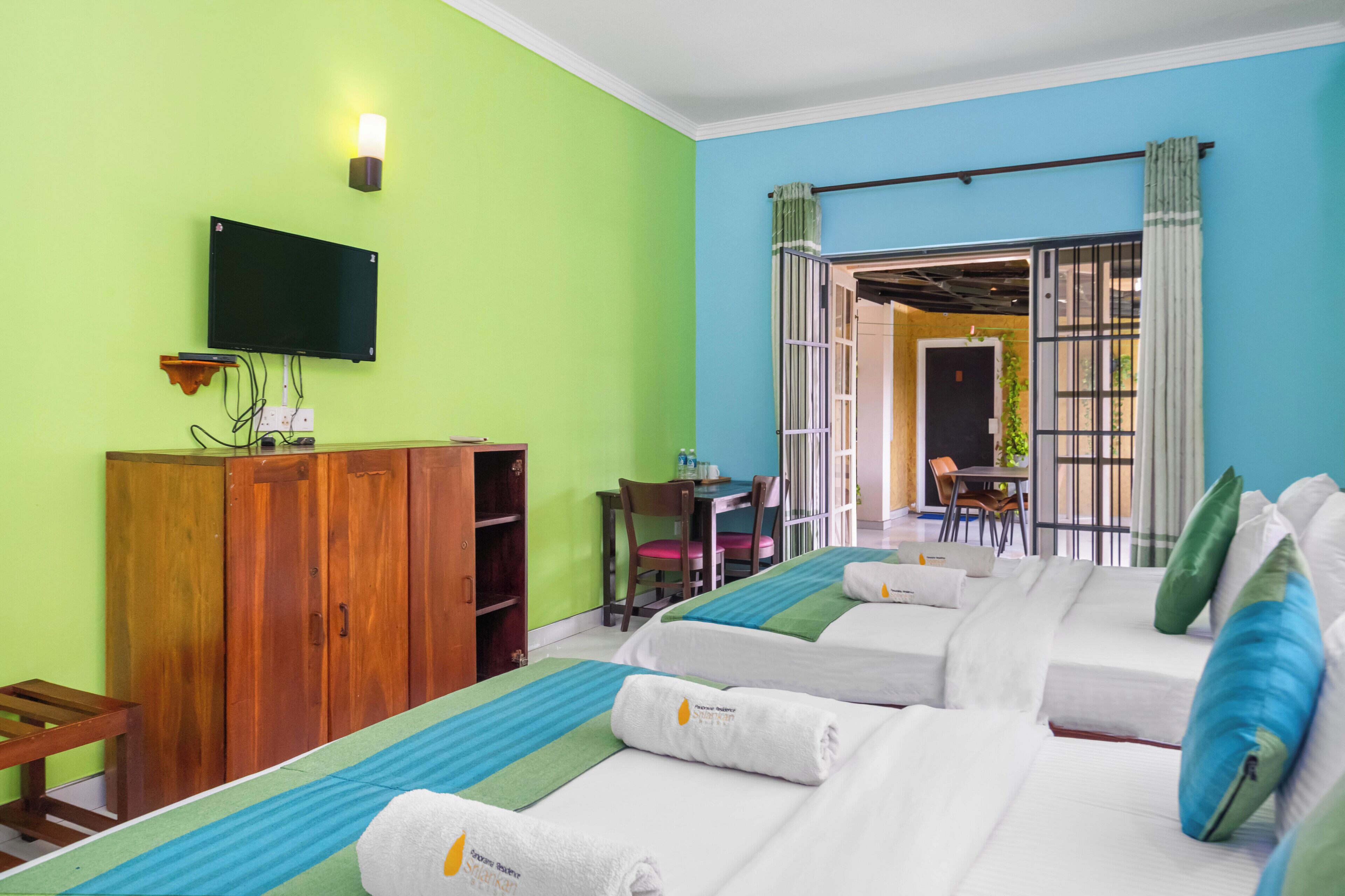 Habitación de hotel con televisión, armario de madera, dos camas con toallas, un escritorio y una silla.