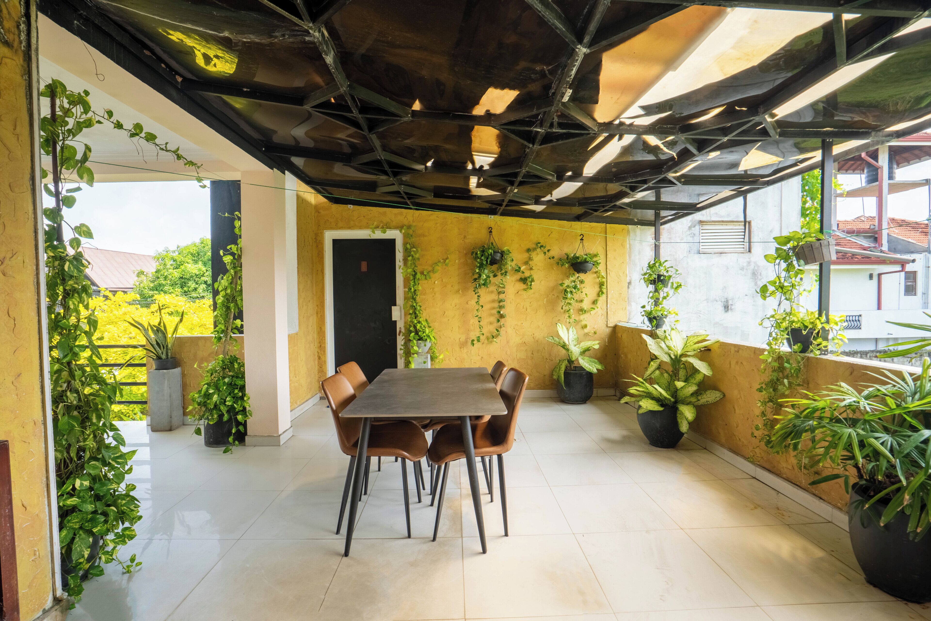 A dining area with a table and chairs, surrounded by potted plants, under a metal roof structure.