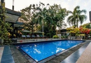 Ein Swimmingpool mit Liegestühlen und einer überdachten Sitzgelegenheit, umgeben von tropischen Pflanzen und Palmen.
