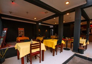 Un restaurante con manteles amarillos y sillas de madera, que presenta un interior oscuro y un suelo de baldosas.