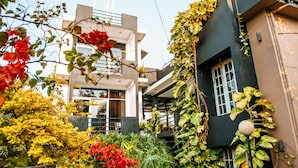 A modern building with a balcony, surrounded by lush greenery and flowering plants.