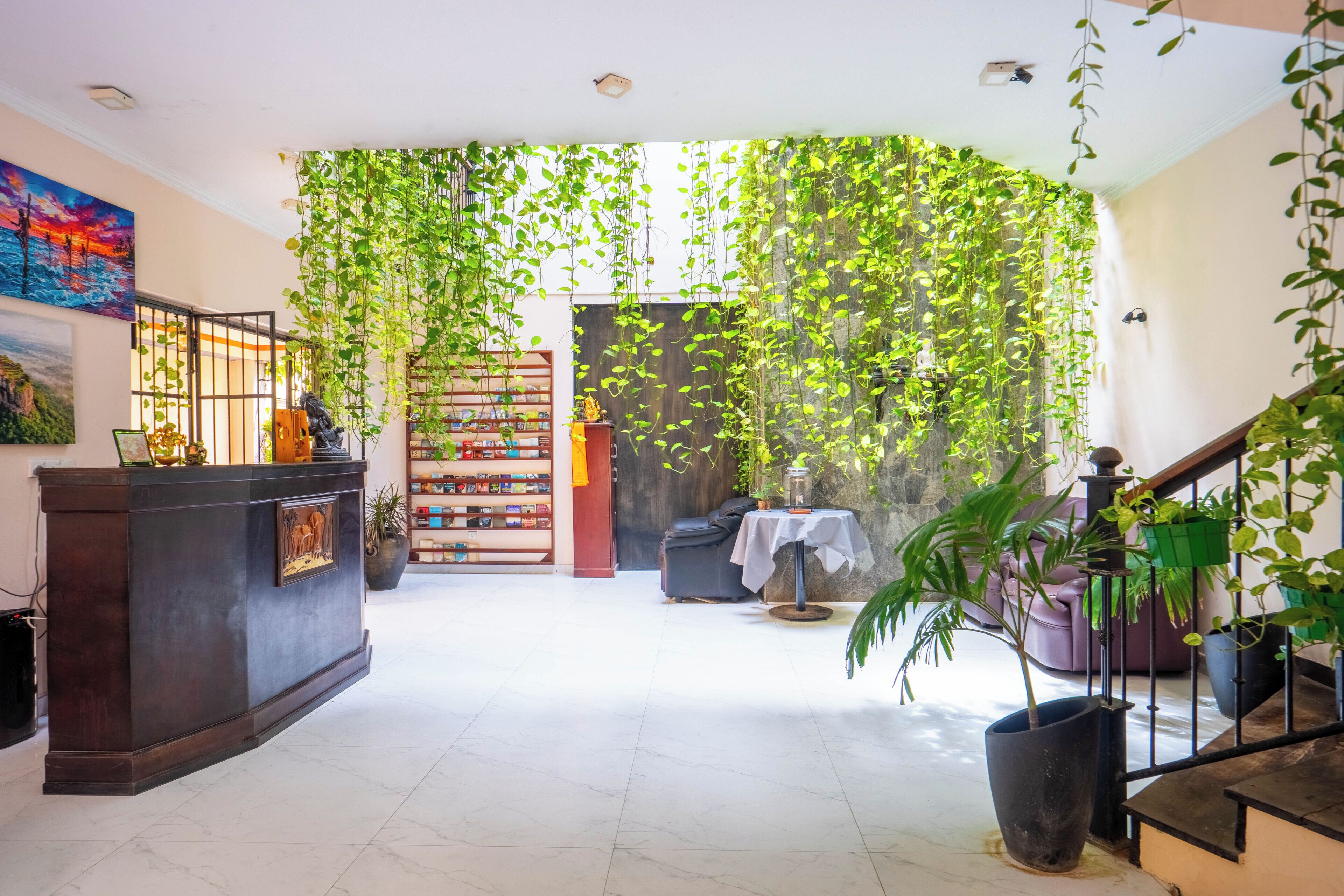A spacious lobby with a reception desk, a bookshelf, a staircase, and hanging plants.
