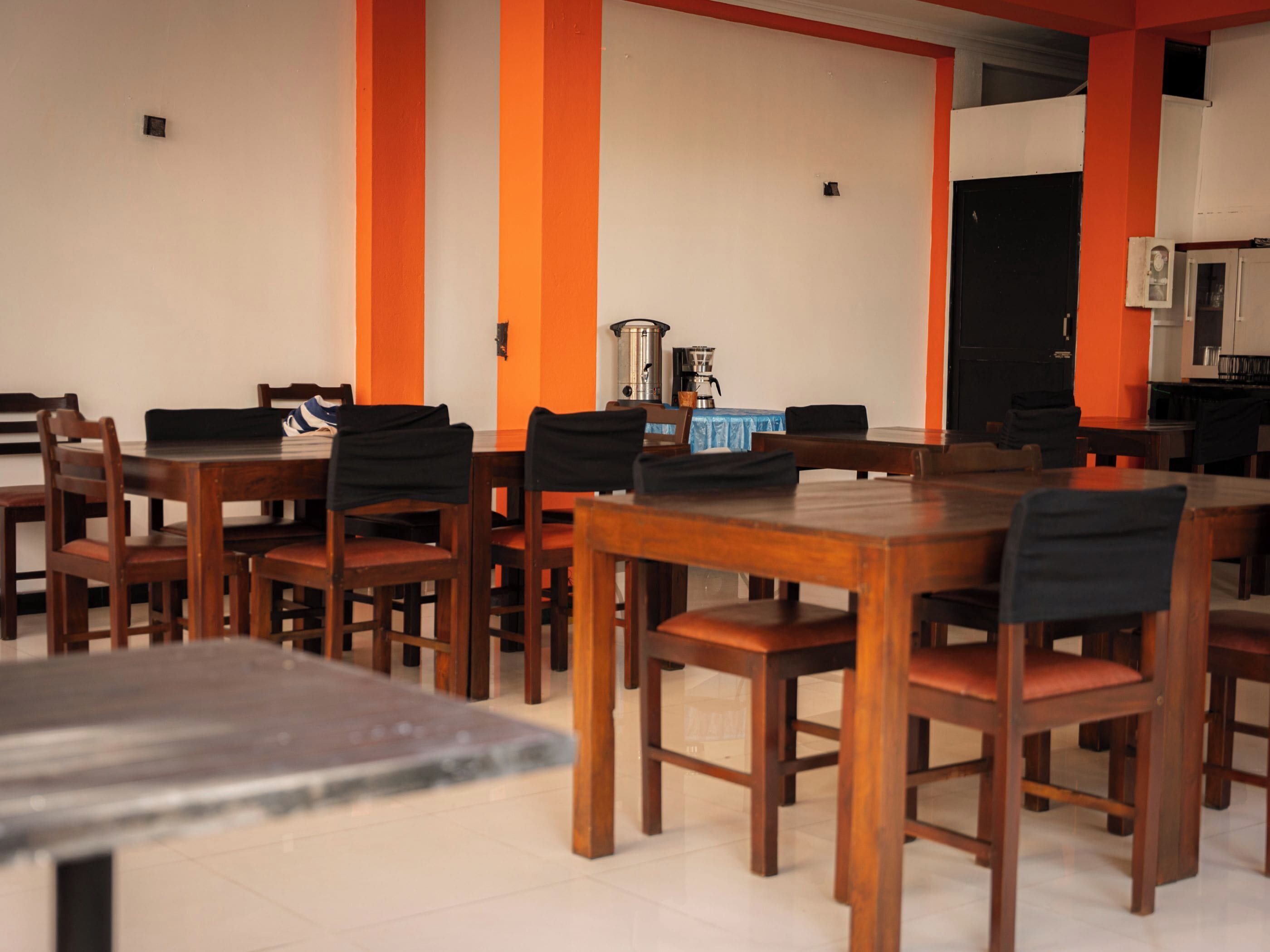 A dining area with wooden tables and chairs, a coffee machine, and a black door in the background.