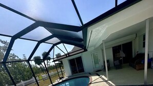 A swimming pool with a clear blue water, surrounded by a brick deck and a glass enclosure. - 4 bed/ 3 bath Villa Heated Pool (Cape Coral)