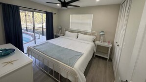 A bedroom with a bed, bedside tables, a ceiling fan, a window with blinds, and a view of a pool outside. - 4 bed/ 3 bath Villa Heated Pool (Cape Coral)