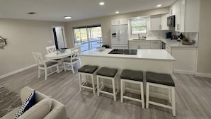 A modern kitchen with white cabinetry, a central island with bar stools, and a dining area with a white table and chairs. - 4 bed/ 3 bath Villa Heated Pool (Cape Coral)