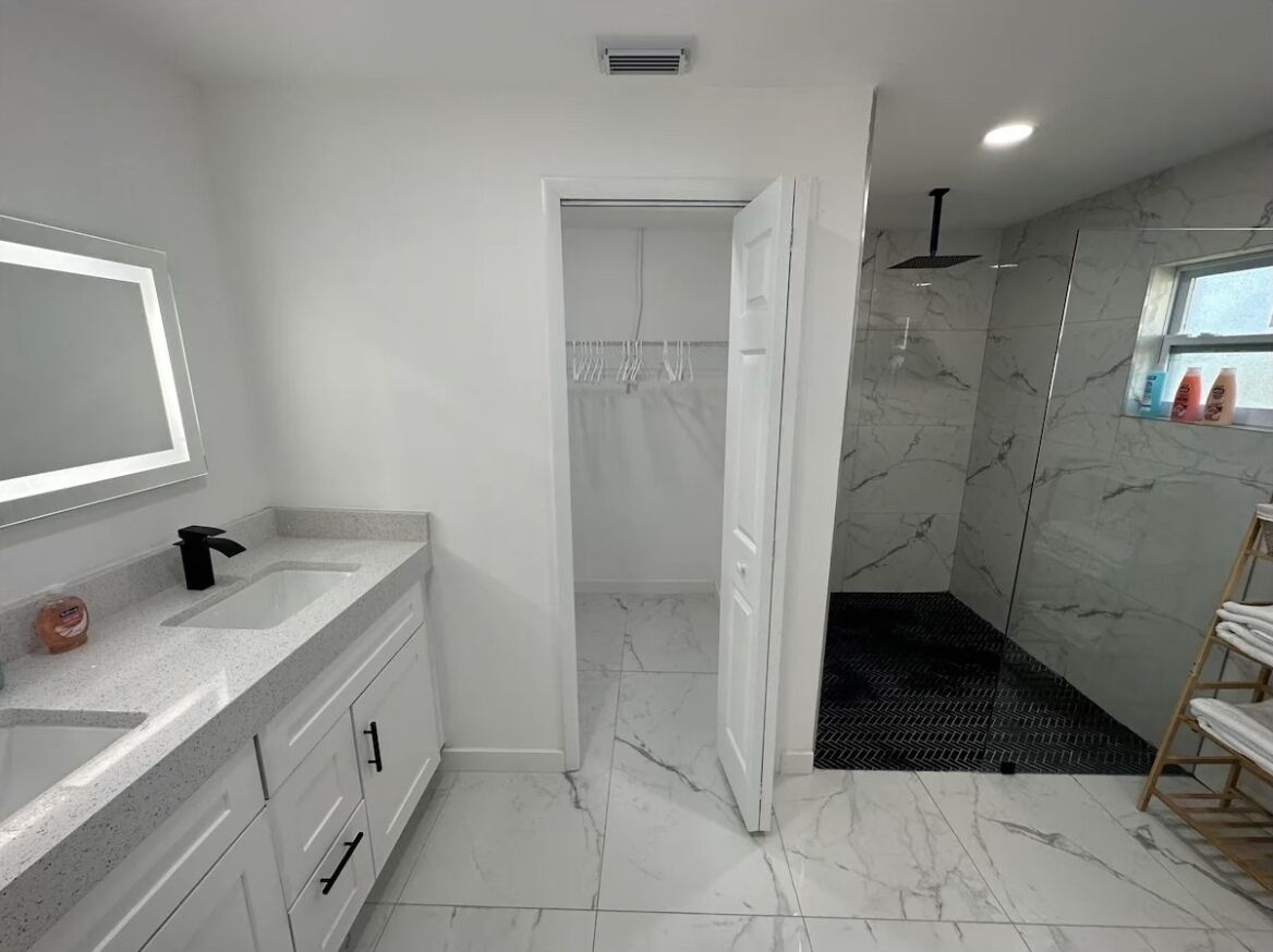 A modern bathroom with a marble floor, a large mirror, a shower area, and a vanity with a sink and cabinets.
