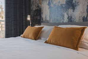 A bed with white linens and two brown pillows, a white bedside lamp, and a stone-patterned curtain. - Exclusive Suite with Terrace/Ultra Wi-fi/Free Parking (Trieste)