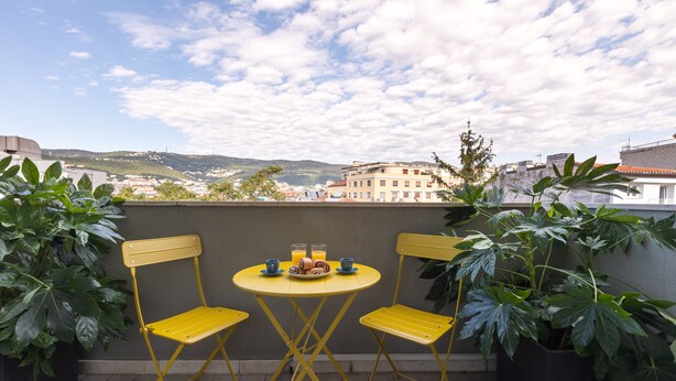 Una mesa amarilla y dos sillas amarillas en un balcón con vista a la ciudad.