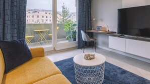 Una sala de estar moderna con un sofá, una mesa redonda de centro, un televisor y un balcón con sillas amarillas y una planta.