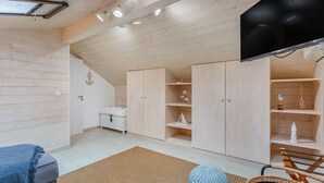 A room with wooden walls and ceiling, a television mounted on the wall, and a bed with a blue blanket.