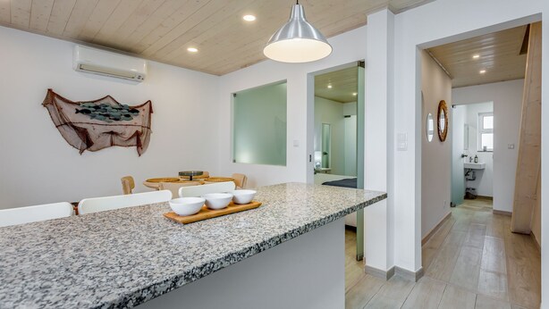 A modern kitchen with granite countertops, a central island with bowls, a hanging light fixture, and a wall-mounted air conditioner.