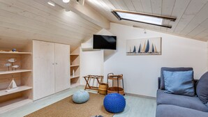 A modern living room with wooden floors, a grey sofa, a flat-screen TV mounted on the wall, and a nautical-themed painting.