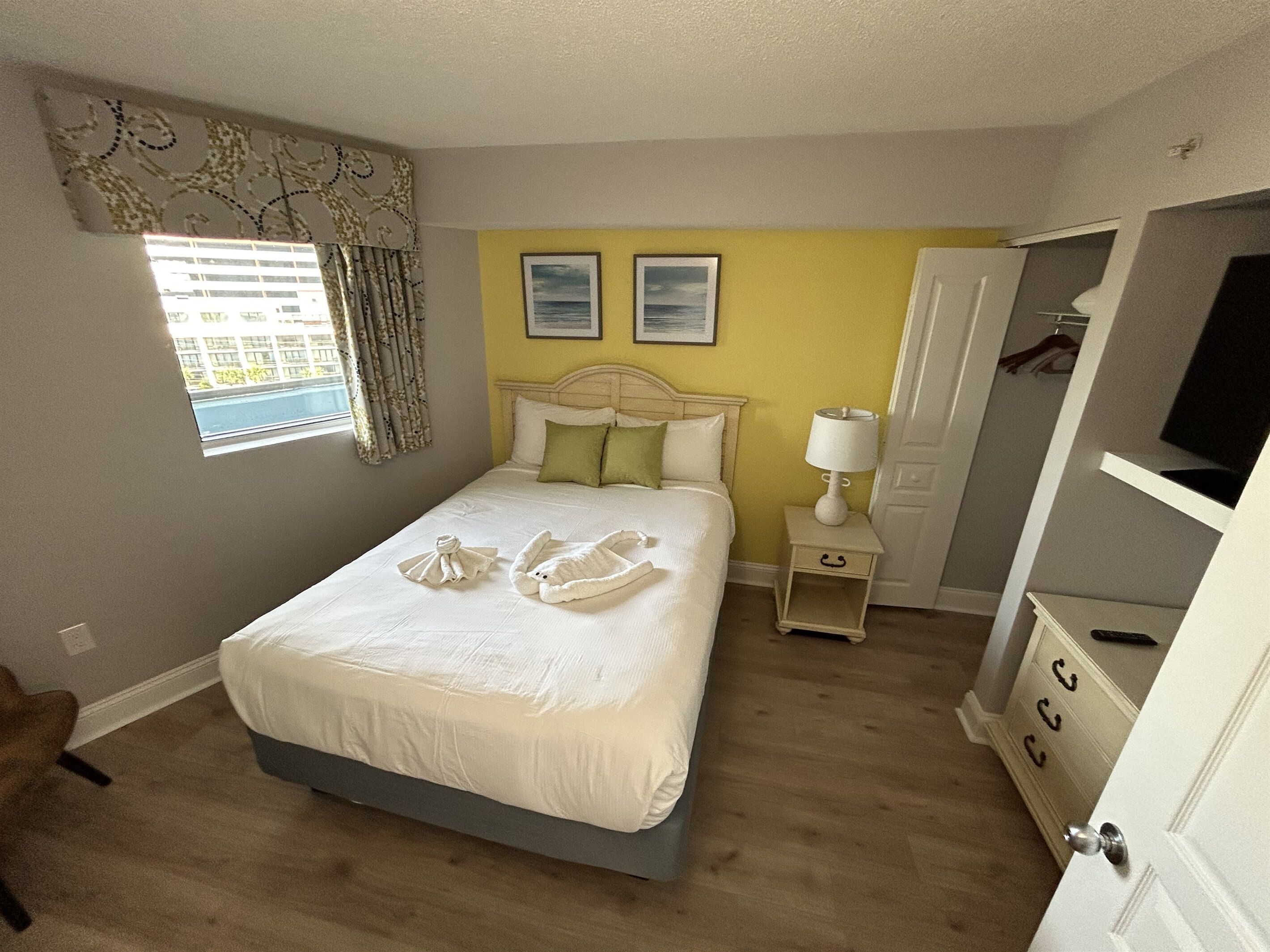 Une chambre à coucher avec un lit, une table de chevet, une lampe, une armoire et une fenêtre avec des rideaux.