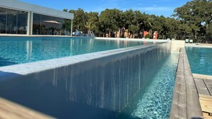 A swimming pool with a wooden deck and a modern building in the background. - Mini Villa T3 de 48m2 (Lecci)