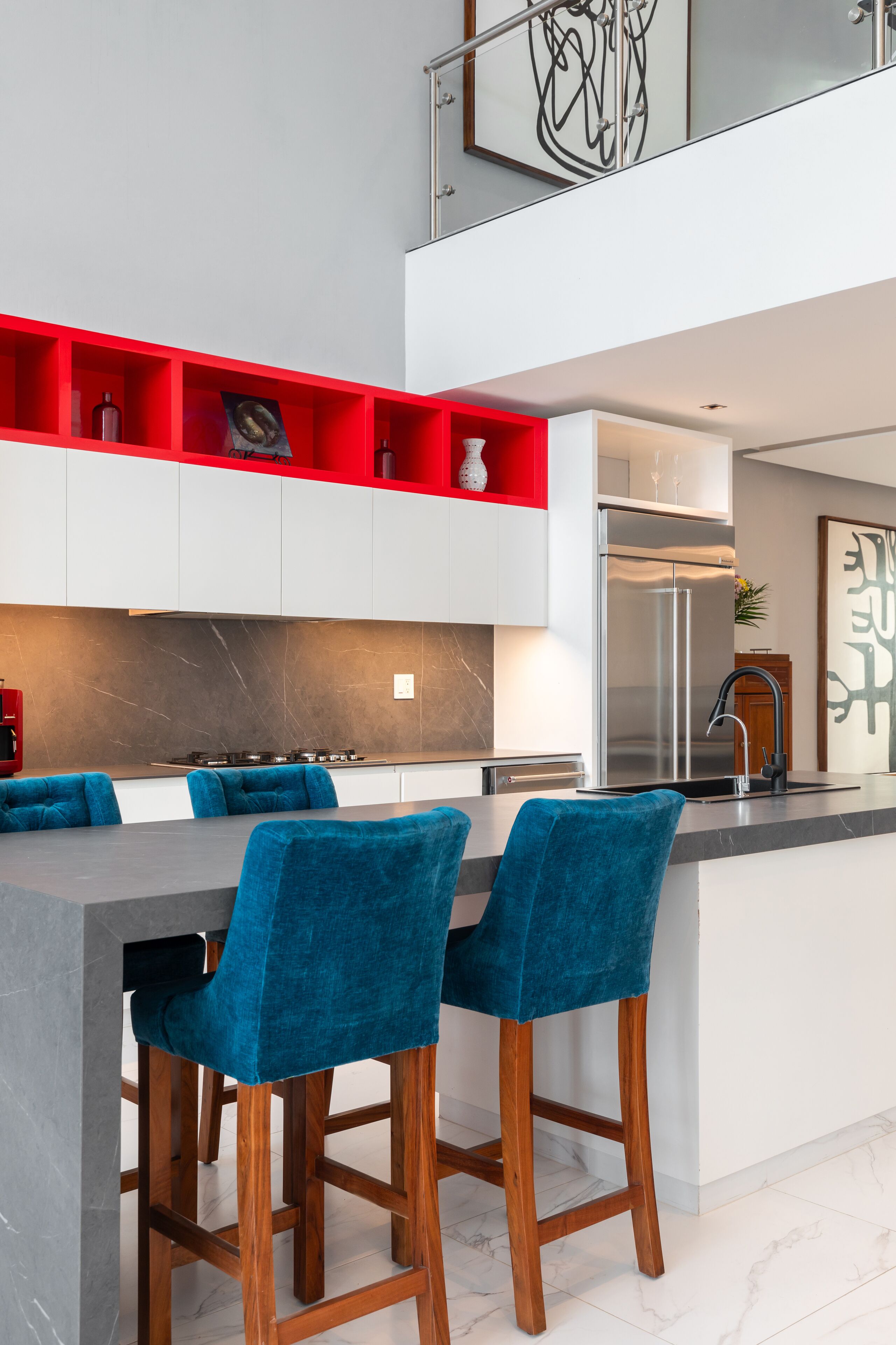 Une cuisine moderne avec un îlot central, des étagères rouges et des tabourets de bar bleus.