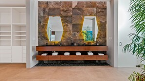 A modern bathroom with a stone wall, two sinks, and a wooden vanity. - Villa E11even With Private Chef Ocean Front (isla mujeres)