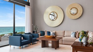A modern living room with a large window overlooking the ocean, a beige sofa, a blue armchair, and a wooden coffee table. - Villa E11even With Private Chef Ocean Front (isla mujeres)
