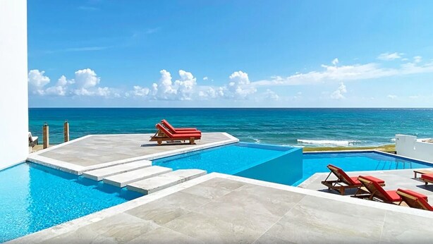 A pool area with clear blue water, a red lounge chair, and a view of the ocean. - Villa E11even With Private Chef Ocean Front (isla mujeres)