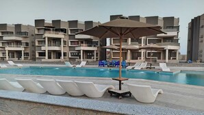 Une piscine entourée d’immeubles à plusieurs étages, avec des chaises longues et des parasols.