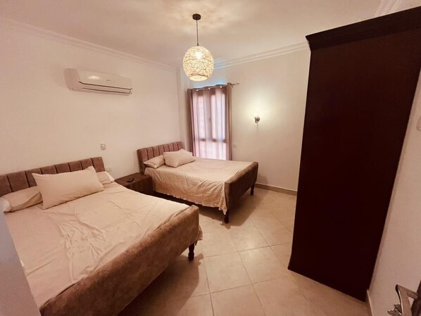 Een hotelkamer met twee bedden, een plafondventilator, een airconditioning en een raam met gordijnen.
