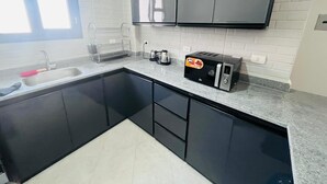 Une cuisine moderne avec des meubles de couleur noire, un plan de travail en granit, un four à micro-ondes encastré et une machine à café.
