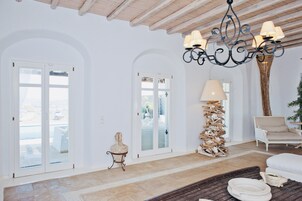 A spacious interior with white walls, a wooden ceiling, and a chandelier. There are large glass doors leading to an outdoor area.