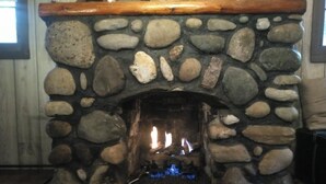 Un camino in pietra con una mensola in legno, un fuoco acceso all'interno e una griglia metallica alla base.